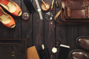 Fashionable male and female personal items with space on a dark wooden background. Leather bag, shoes, watches, luxury, stylish accessories.