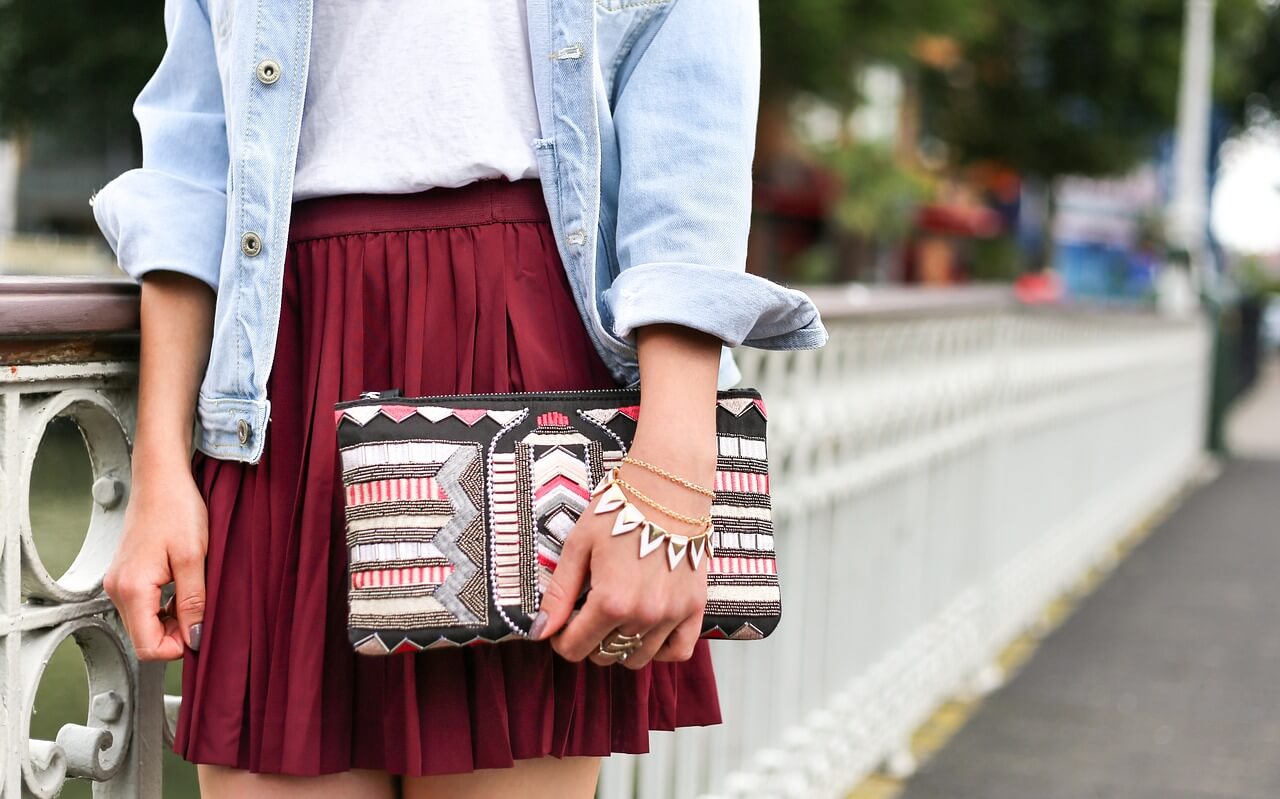 A maroon skirt paired with a light wash jean jacket and patterned purse.